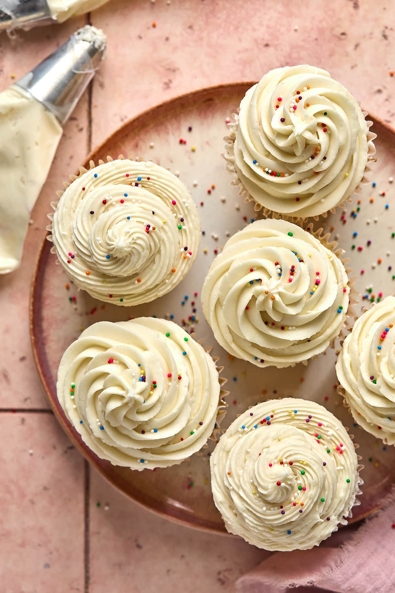 plate of cupcakes with cream-colored frosting piped atop, plus multi-colored sprinkles