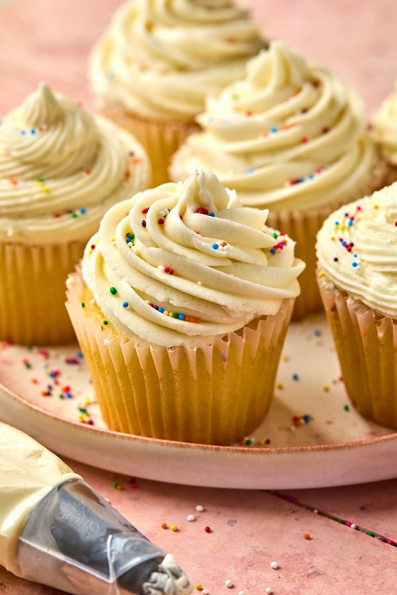 vanilla cupcakes topped with vanilla frosting and multi colored sprinkles