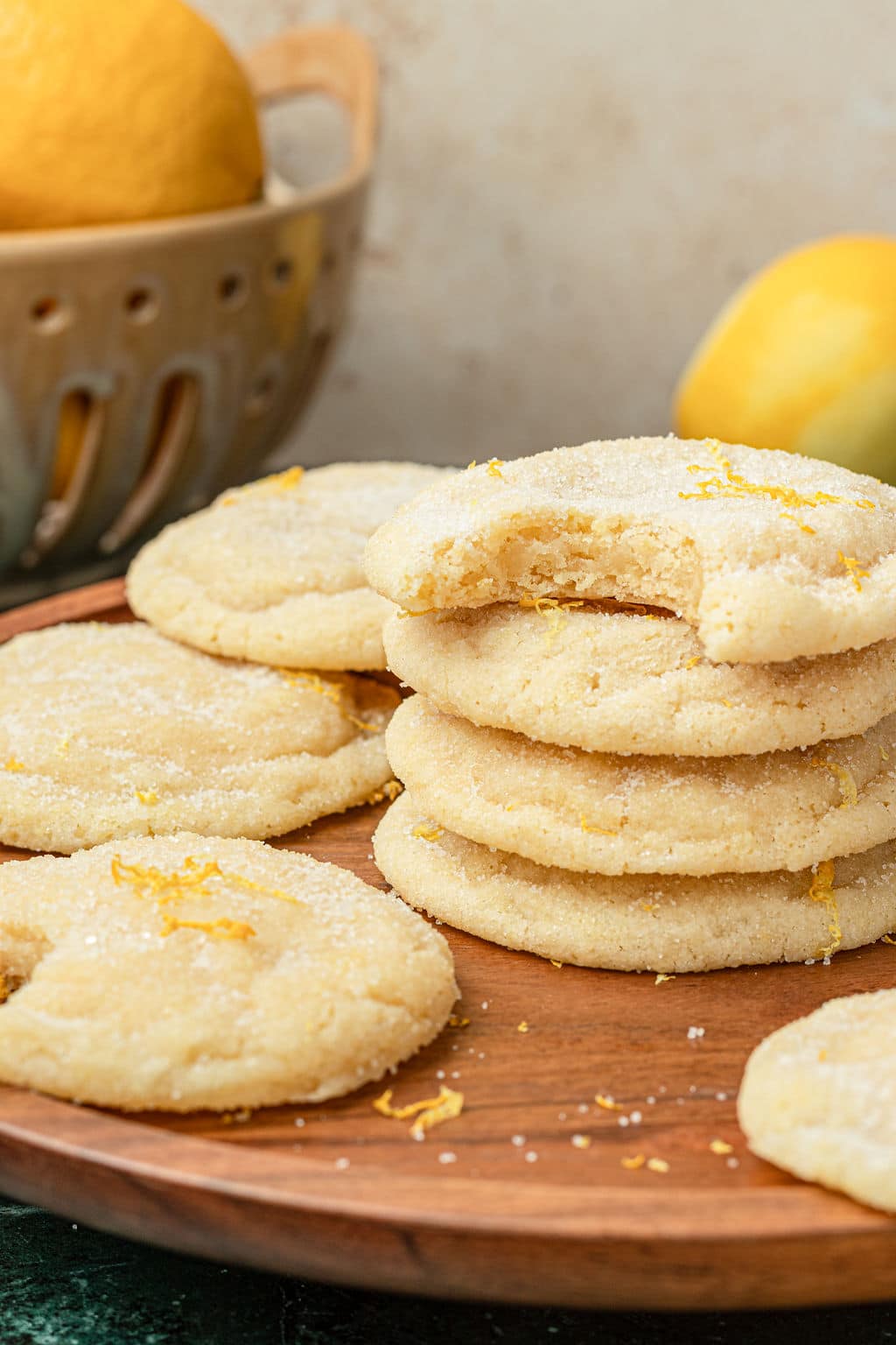 stack of sugar cookeis with lemon zest on a wooden board with lemons in the background