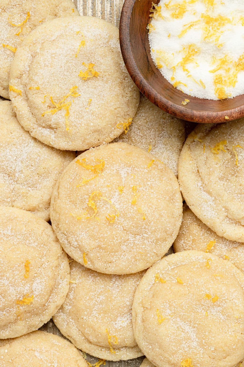 tray of sugar cookies topped with sugar and lemon zest plus a wooden bowl with sugar and lemon zest