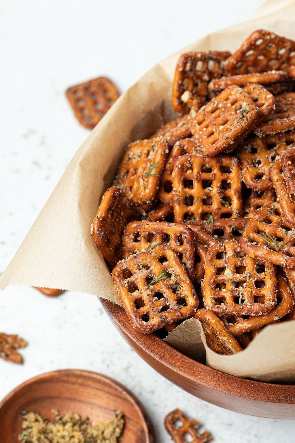 bowl lined with parchment paper and filled with square shaped crisscross pretzels and seasonings