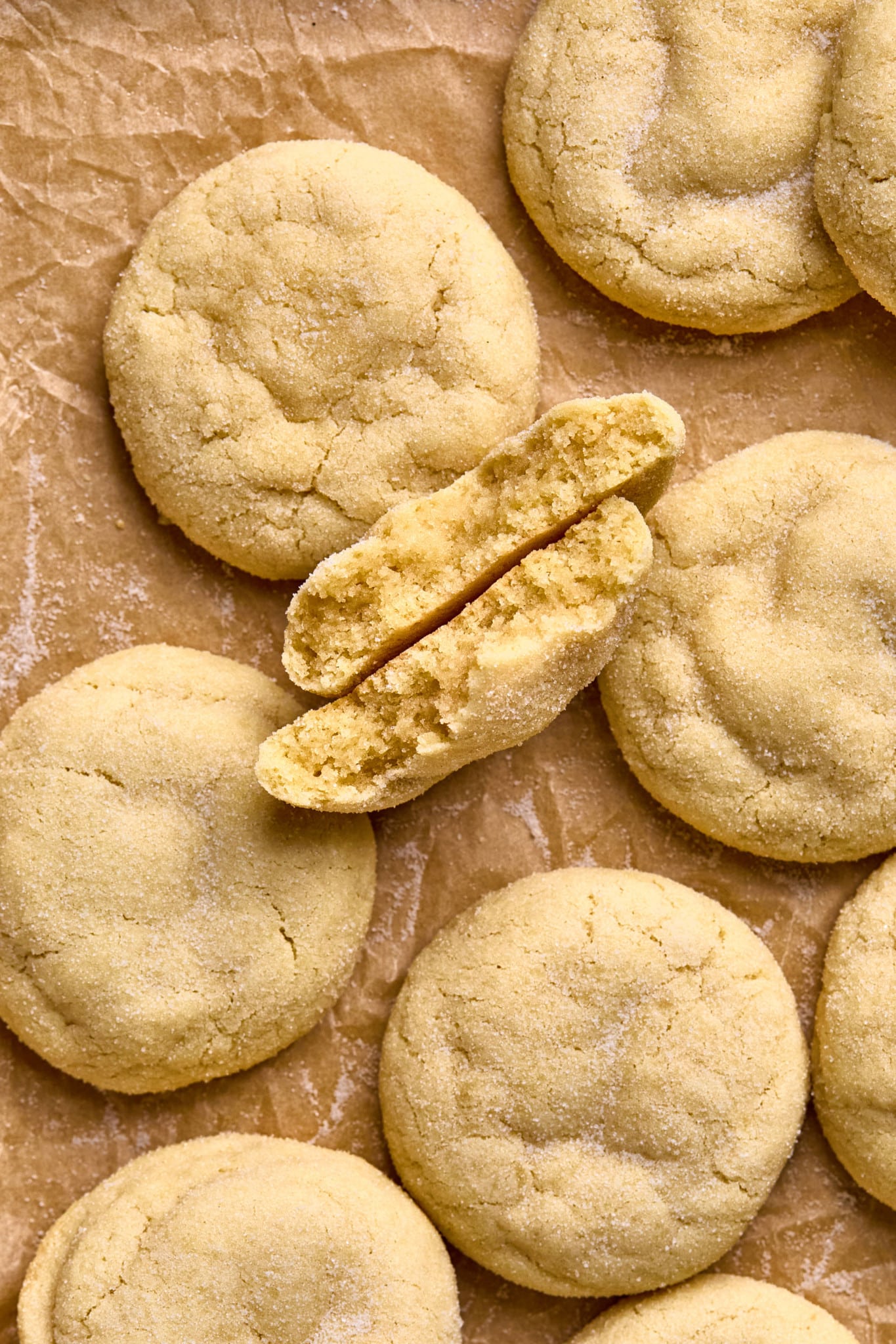 sugar cookies on parchment paper with one cookie broken in half with broken halves facing up