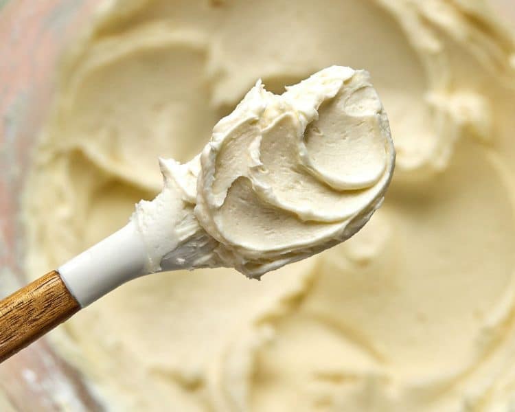 white spatula showing a small amount of vanilla frosting, with bowl of frosting in the background