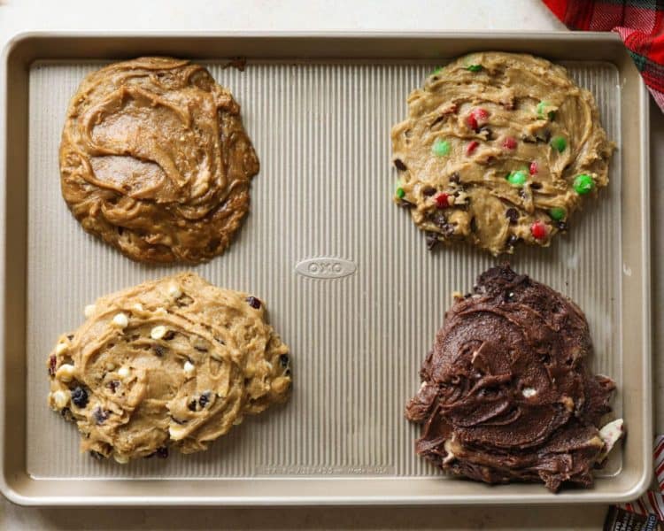 gold cookie sheet with four sections of cookie dough. top left is gingerbread, top right is m&ms, bottom left is white chocolate cranberry, bottom right is chocolate peppermint