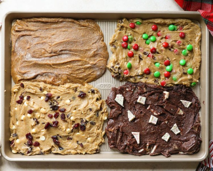 gold cookie sheet with four sections of cookie dough. top left is gingerbread, top right is m&ms, bottom left is white chocolate cranberry, bottom right is chocolate peppermint