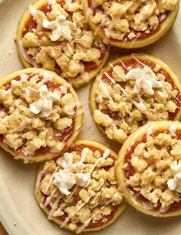 plate with slightly stacked sugar cookies with a pumpkin filling, crumble streusel, icing glaze, and dollop of whipped cream