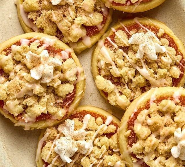 plate with slightly stacked sugar cookies with a pumpkin filling, crumble streusel, icing glaze, and dollop of whipped cream