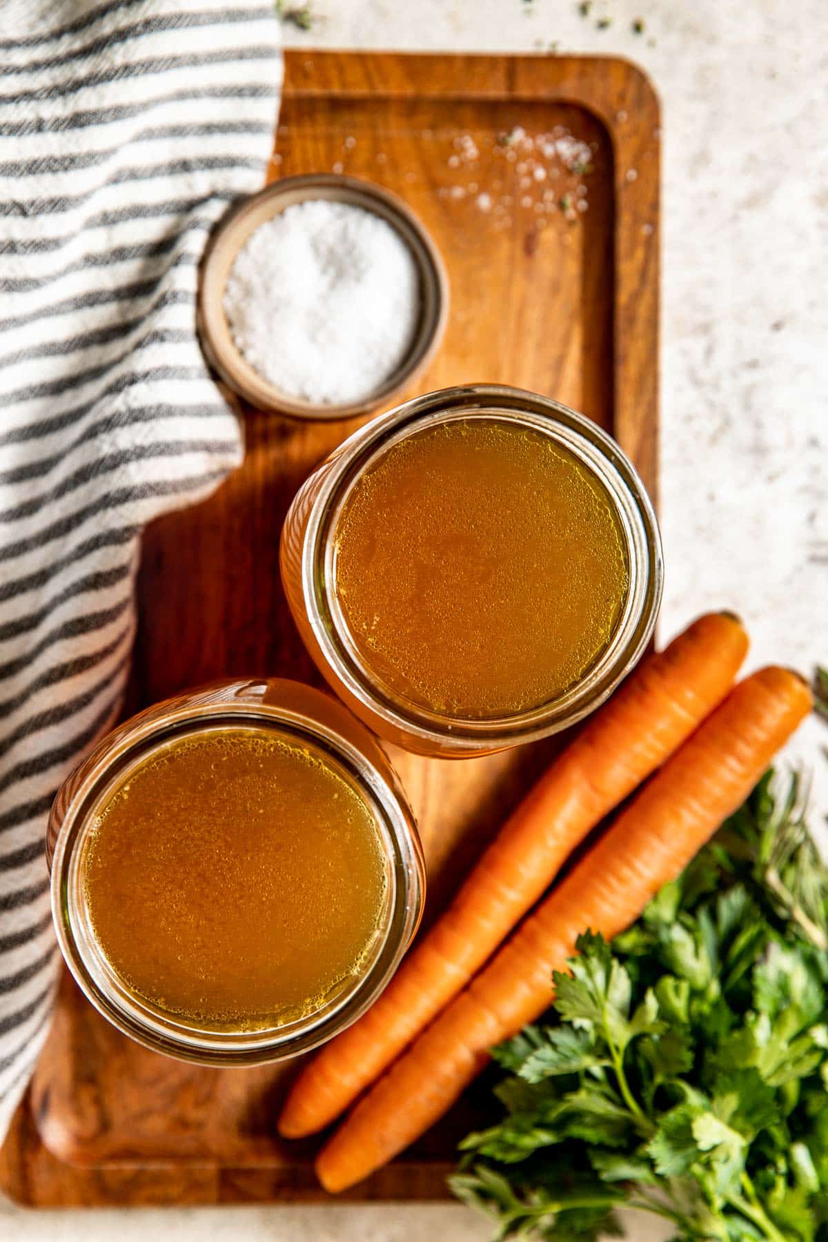 two jars of homemade chicken stock on cutting board