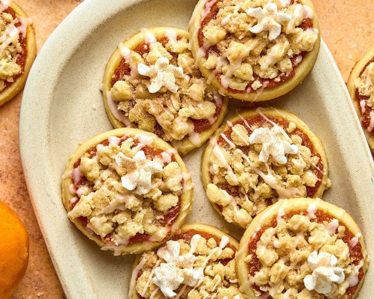 circular pumpkin pie cookies with a glaze and whipped cream dollop on a tan plate