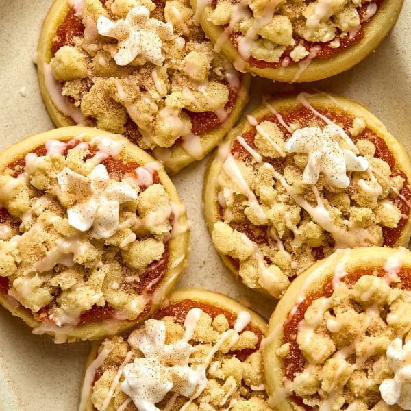plate with slightly stacked sugar cookies with a pumpkin filling, crumble streusel, icing glaze, and dollop of whipped cream