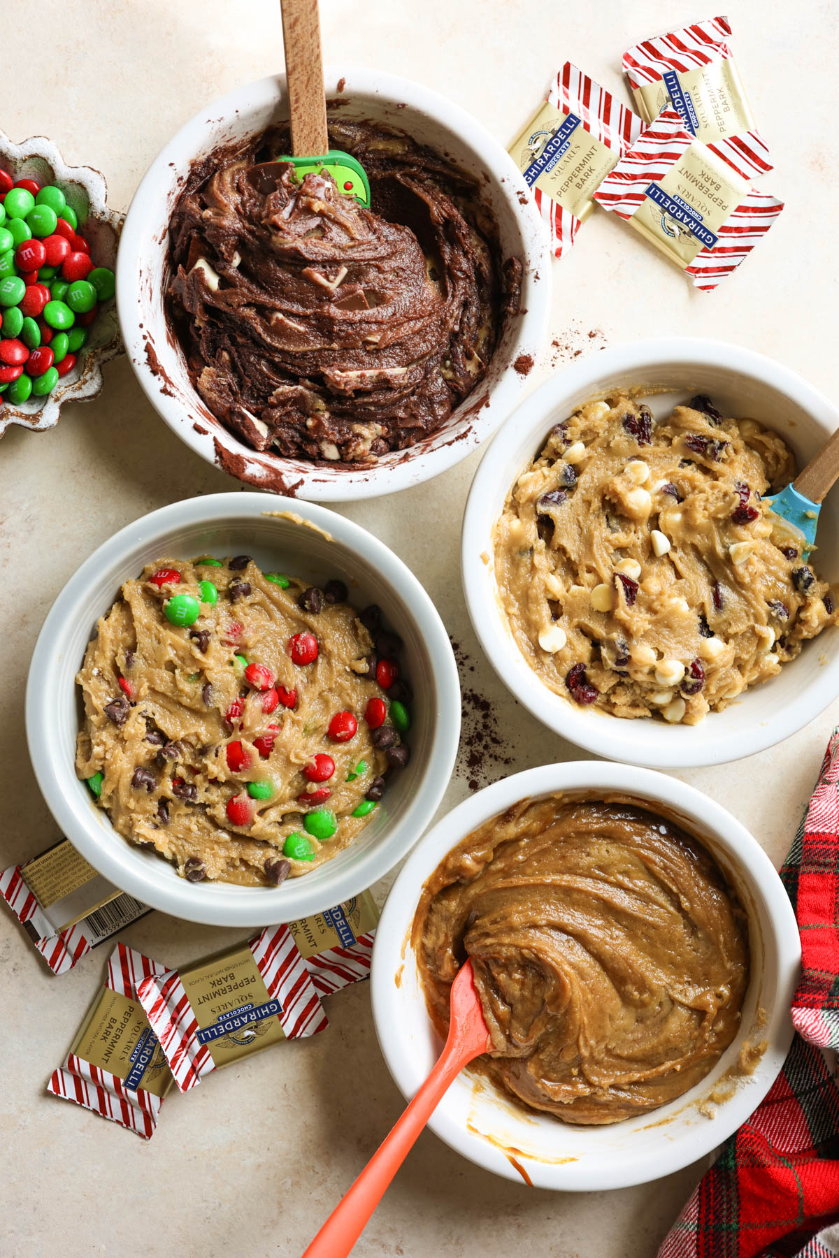 four white ramekins with four different types of cookie dough and two spatulas in two bowls