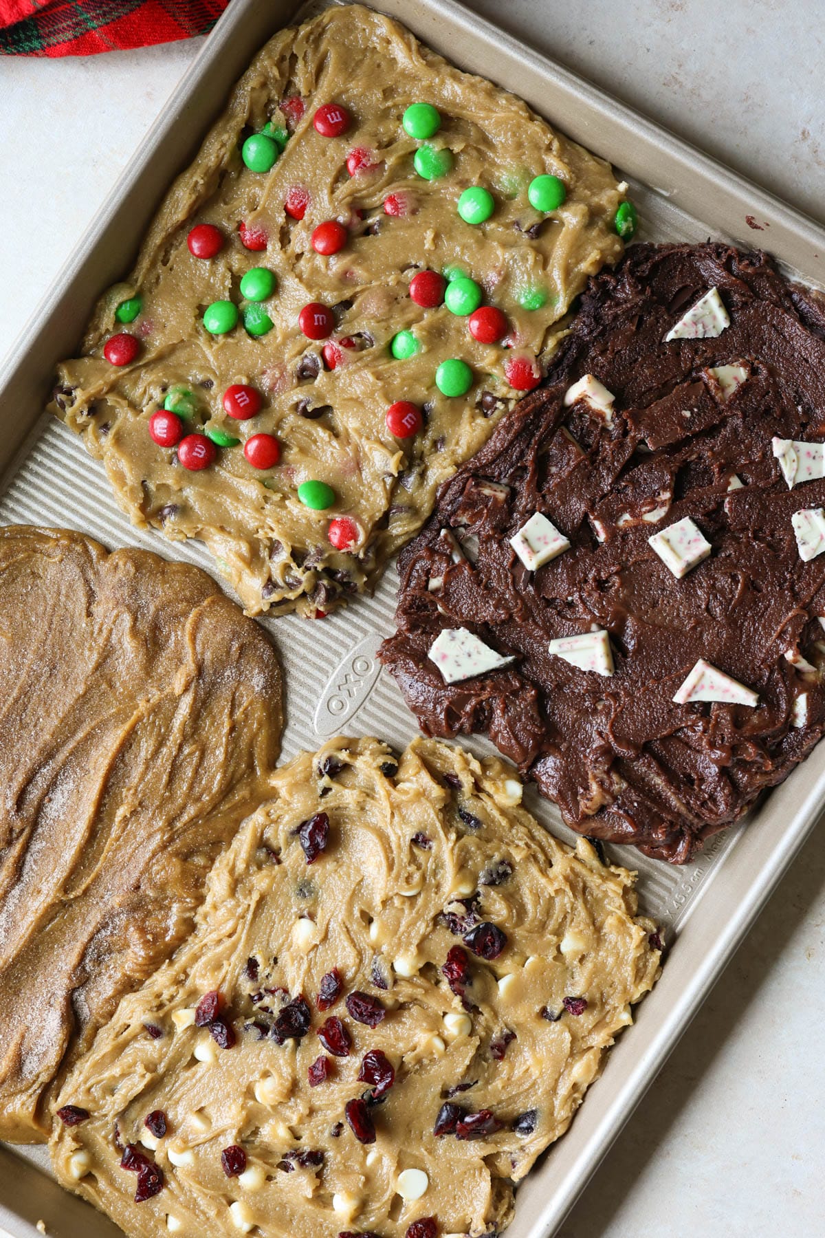 gold OXO sheet pan with four types of cookie dough - gingerbread, m&m, chocolate peppermint, and white chocolate cranberry