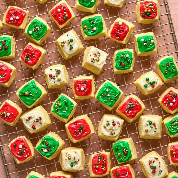 small square cookies with red, white, and green frosting and sprinkles, on a gold cooling rack.