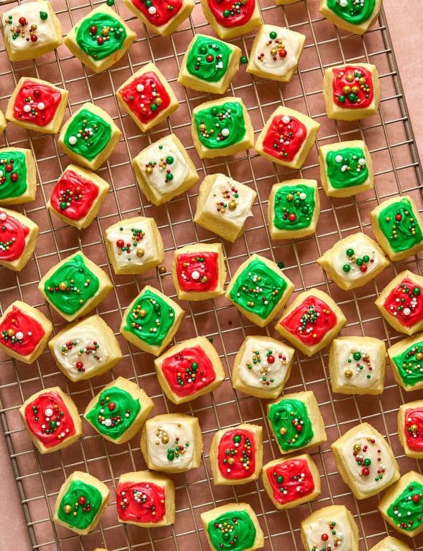 small square cookies with red, white, and green frosting and sprinkles, on a gold cooling rack.