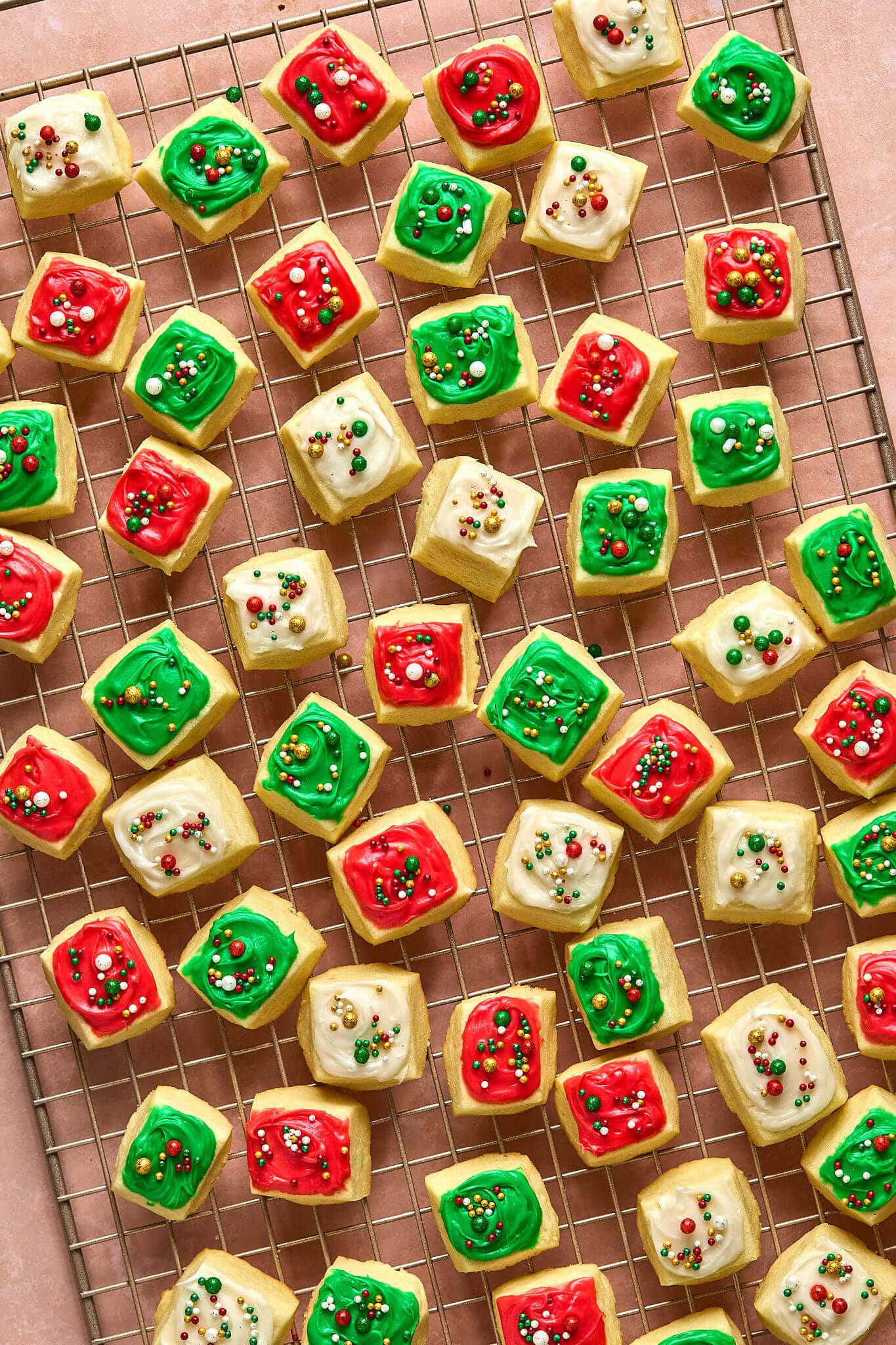 small square cookies with red, white, and green frosting and sprinkles, on a gold cooling rack.