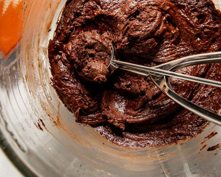 clear bowl with chocolate dough and a cookie scoop.