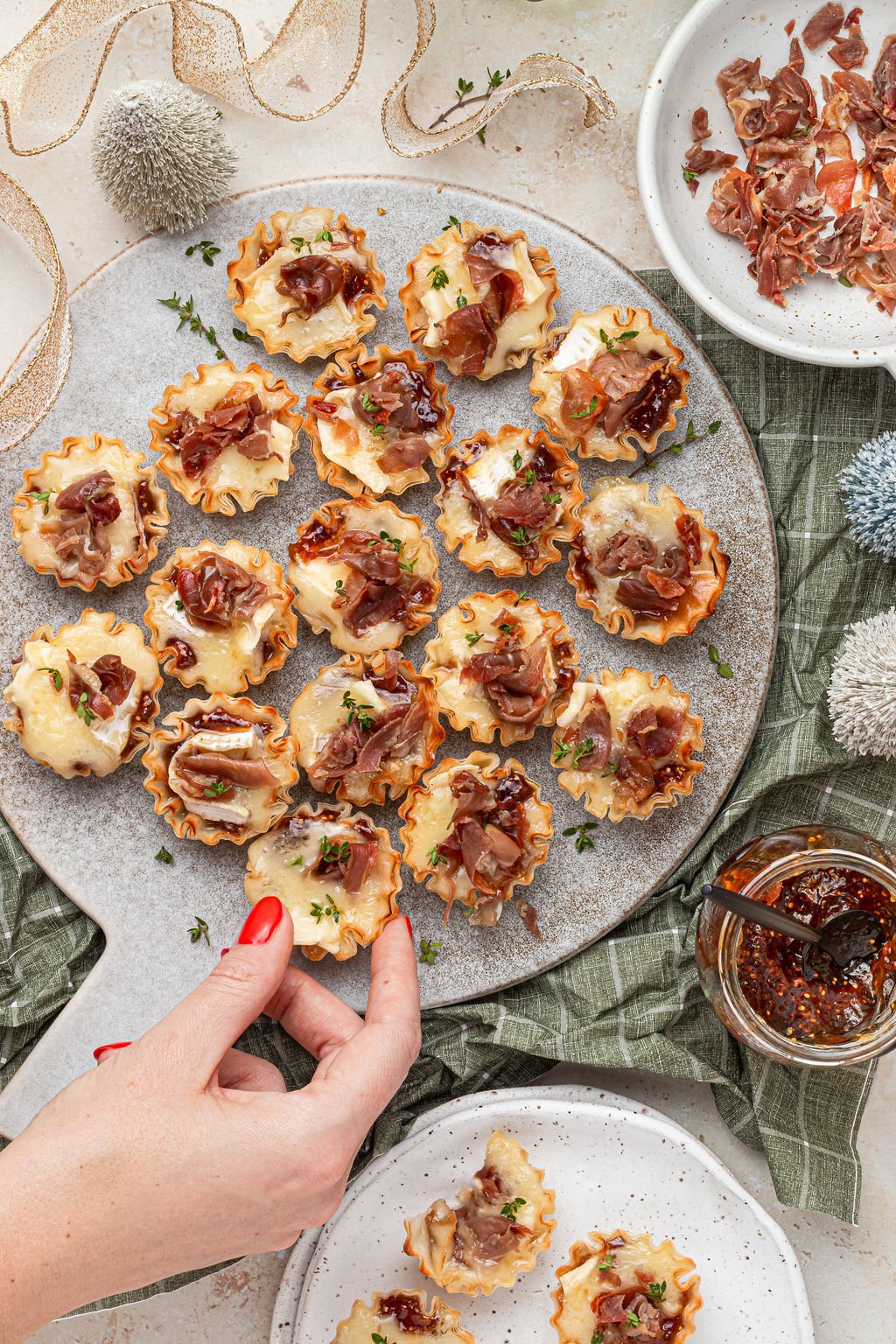 a womans hand grabbing a mini brie bite from a tray. 