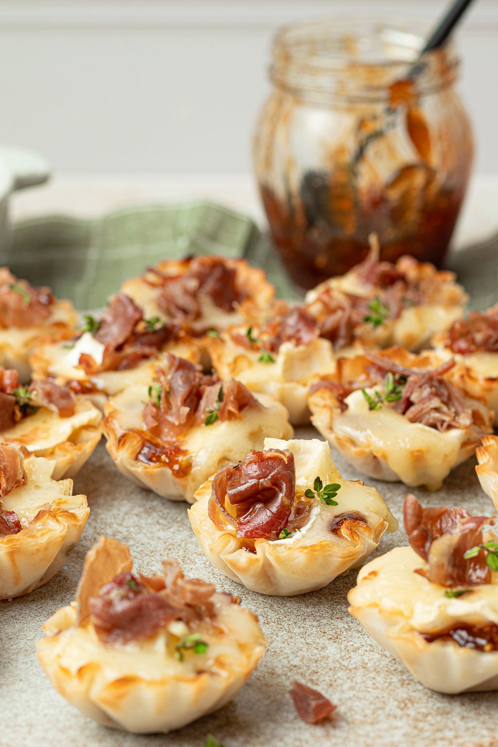 a close up image on mini brie bites in phyllo cups garnished with crispy prosciutto and thyme. 