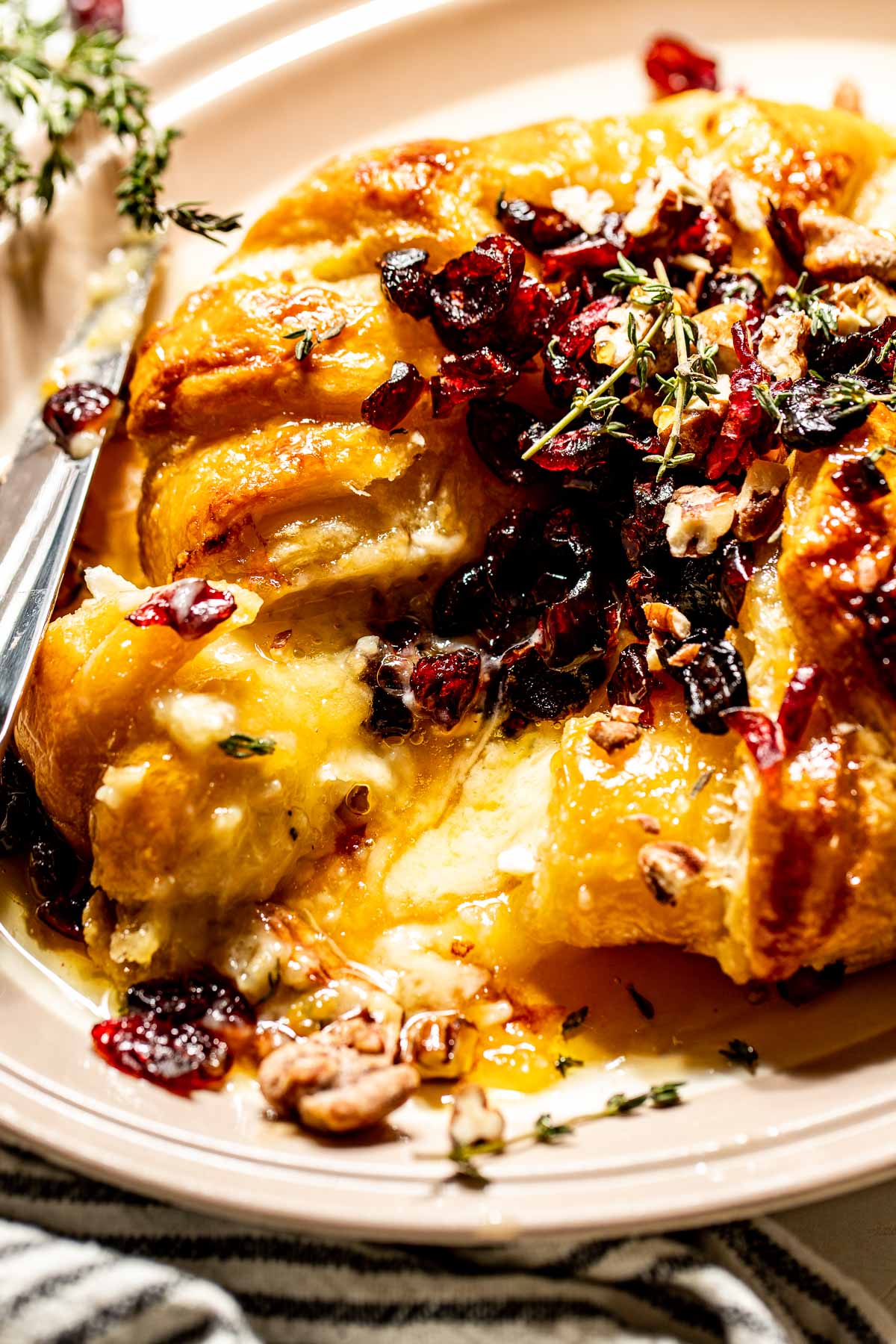 Close up image of a slice of puff-pastry covered baked brie with dried cranberries, candied pecans, thyme, and hot honey.