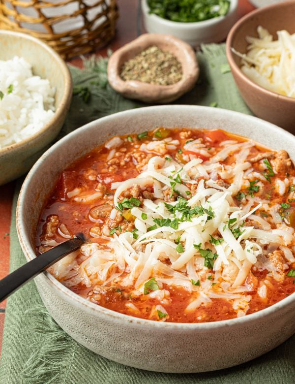 bowl of soup with a red base, chopped veggies, ground beef, white rice, shredded cheese, chopped parsley