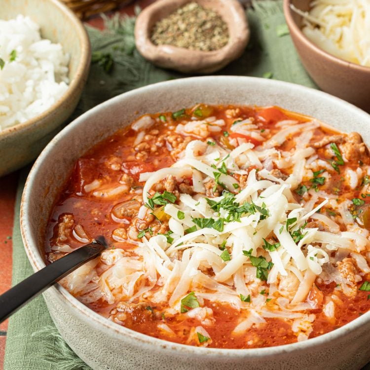 bowl of soup with a red base, chopped veggies, ground beef, white rice, shredded cheese, chopped parsley