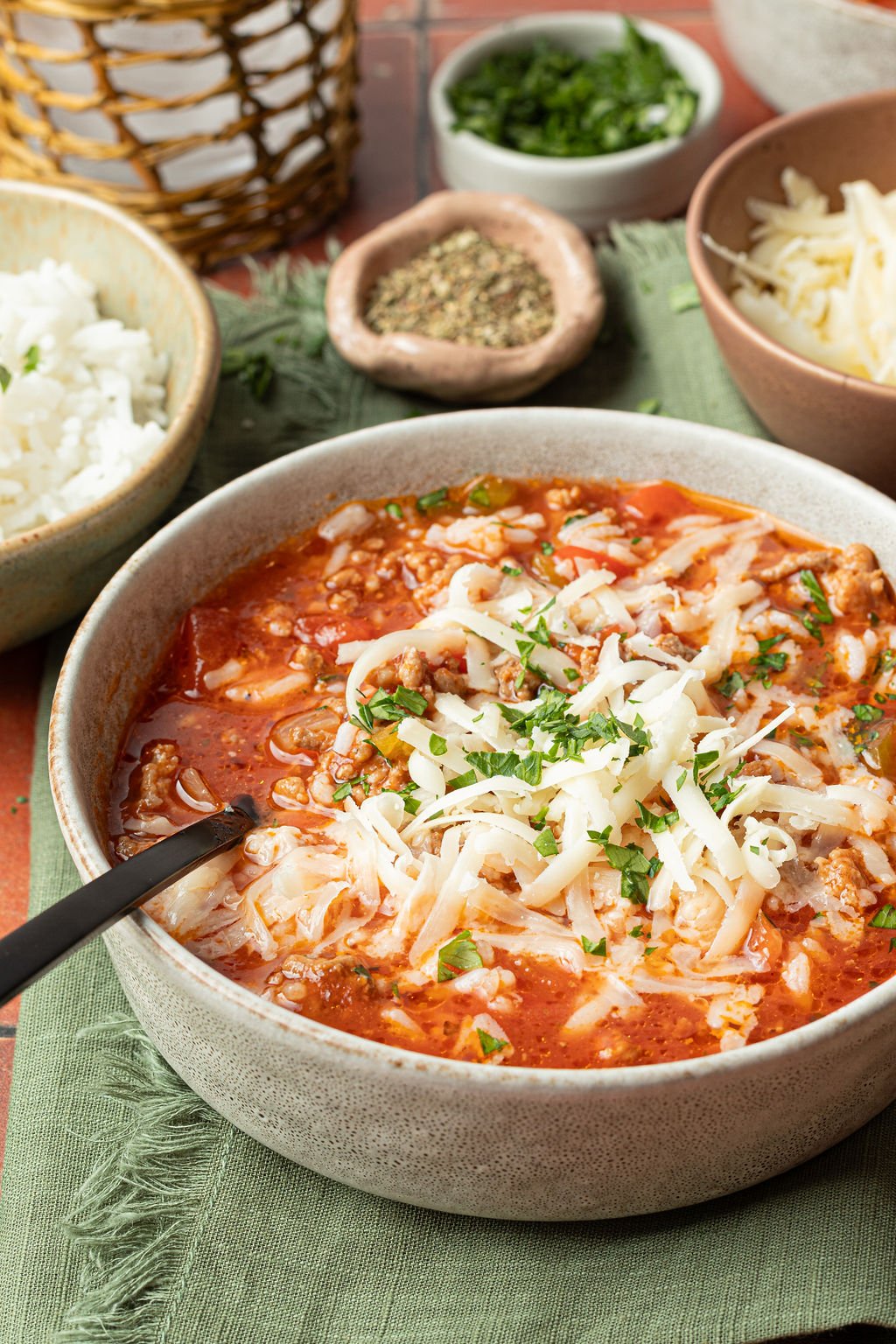 bowl of soup with a red base, chopped veggies, ground beef, white rice, shredded cheese, chopped parsley