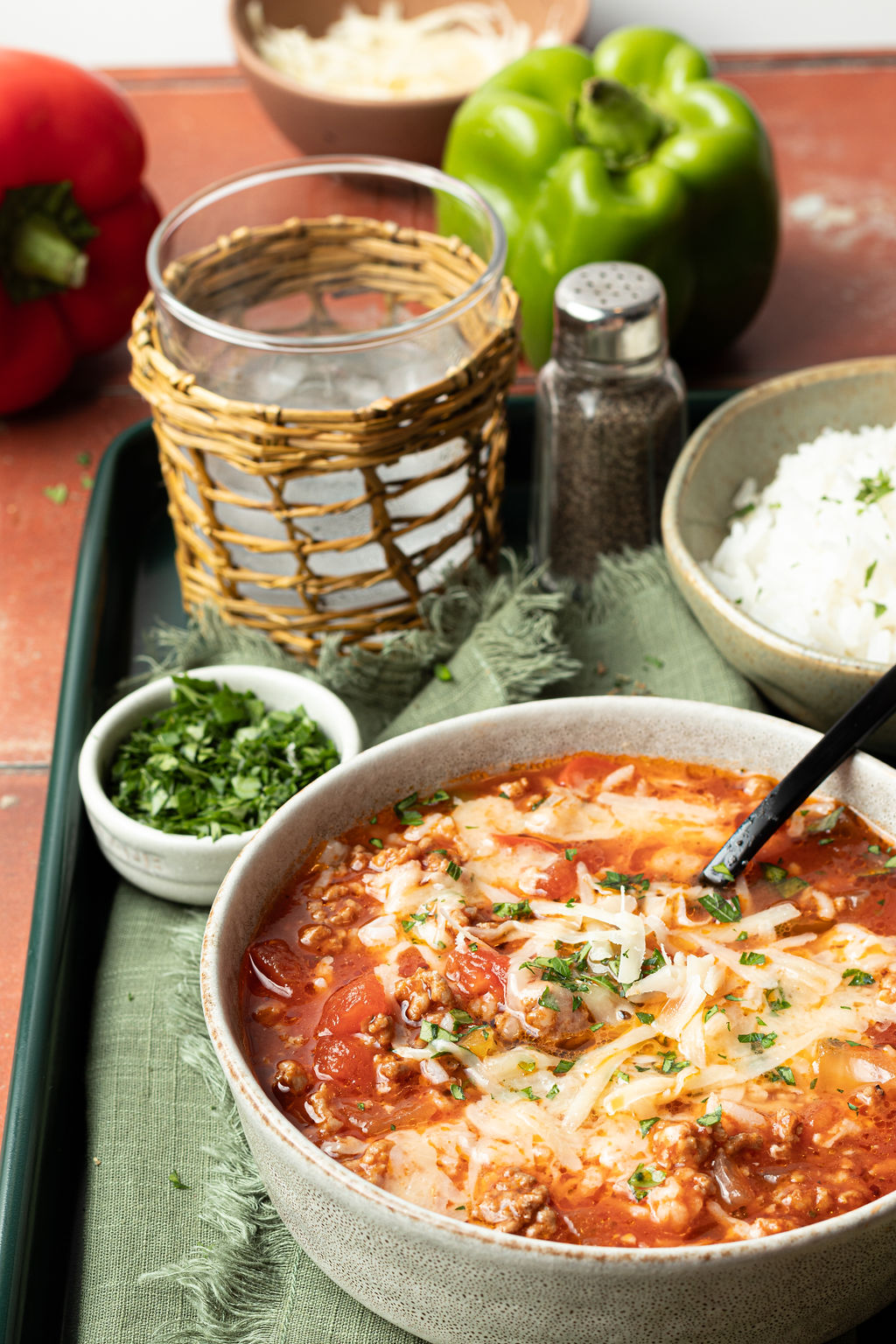 bowl of soup with a red based, ground beef, chopped veggies, topped with white rice and shredded cheese