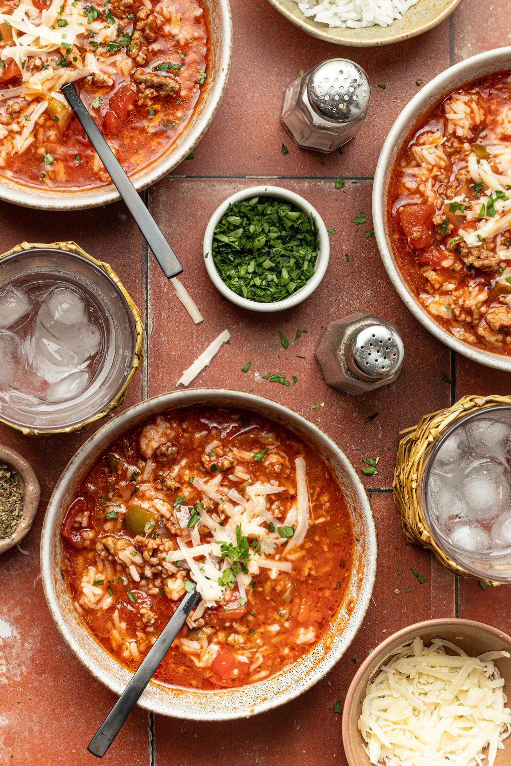 three bowls of stuffed bell pepper soup, small bowl of chopped parsley, glasses of ice water, salt and pepper shakers.