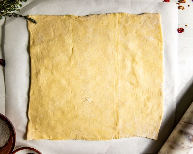 Sheet of unbaked puff pastry rolled out on top of parchment paper.