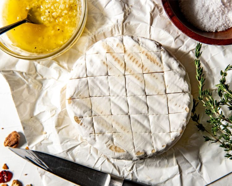 Wheel of brie cheese with criss cross scoring marks.