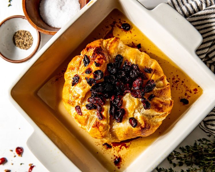 Puff pastry covered brie topped with dried cranberries in a white, square baking dish.