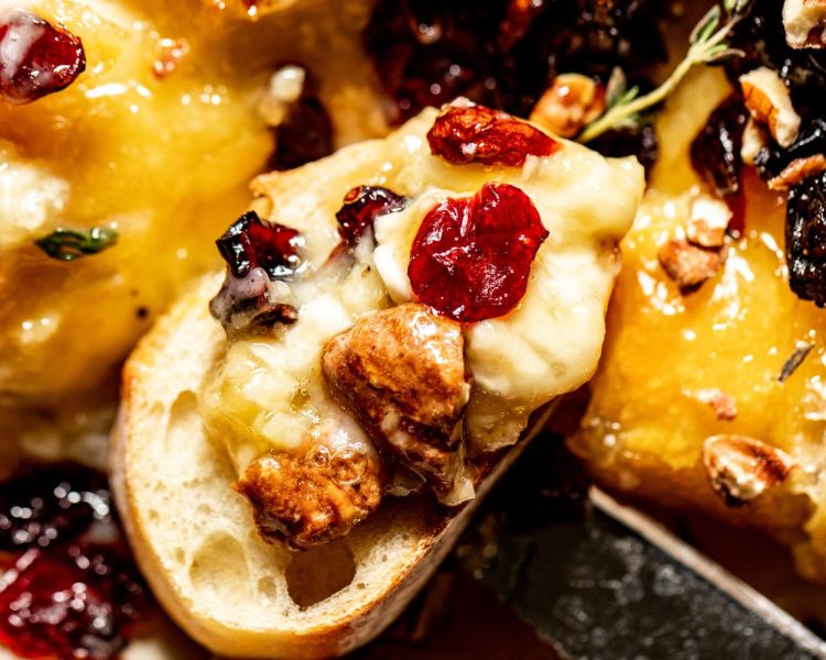 Slice of baguette topped with baked brie, candied pecans, dried cranberries, and hot honey.