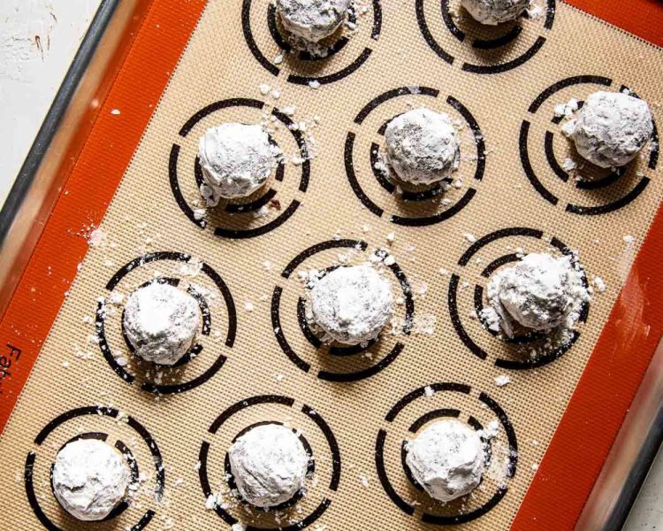 cookie dough balls rolled in powdered sugar on a silpat baking sheet before baking.