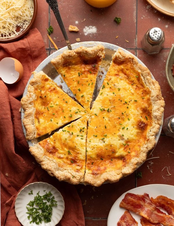 Whole baked quiche topped with green onion in a silver pie pan with small pieces missing.