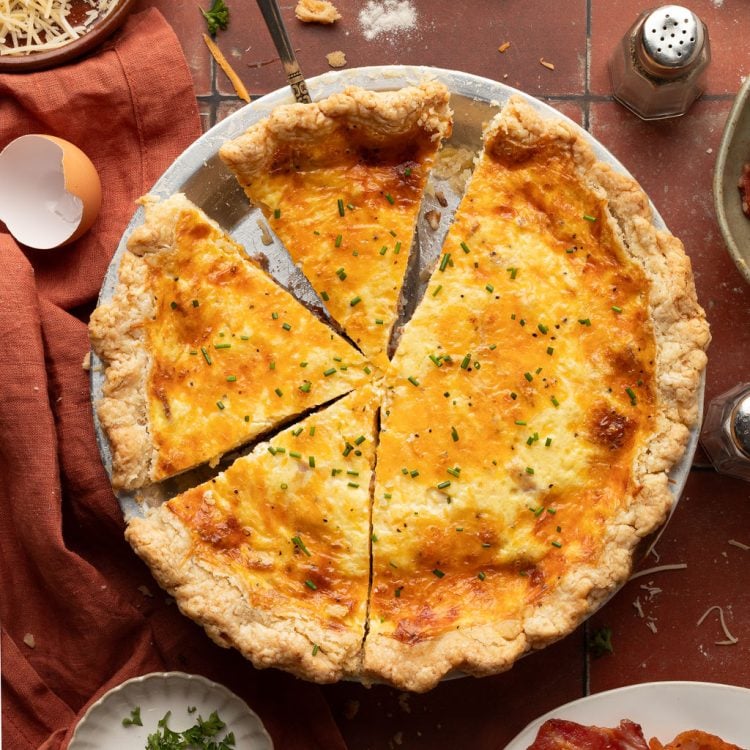 Whole baked quiche topped with green onion in a silver pie pan with small pieces missing.