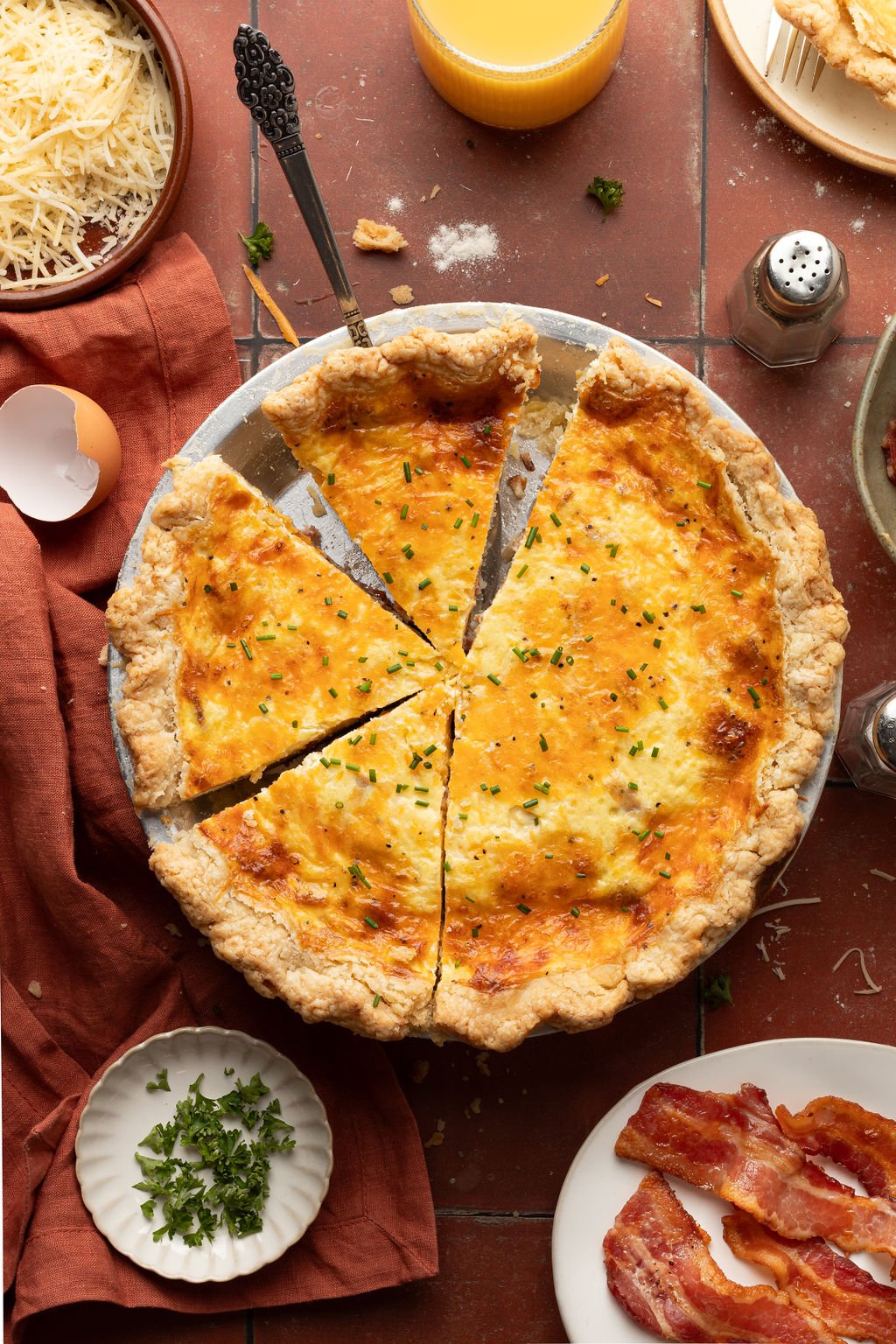 Whole baked quiche topped with green onion in a silver pie pan with small pieces missing.