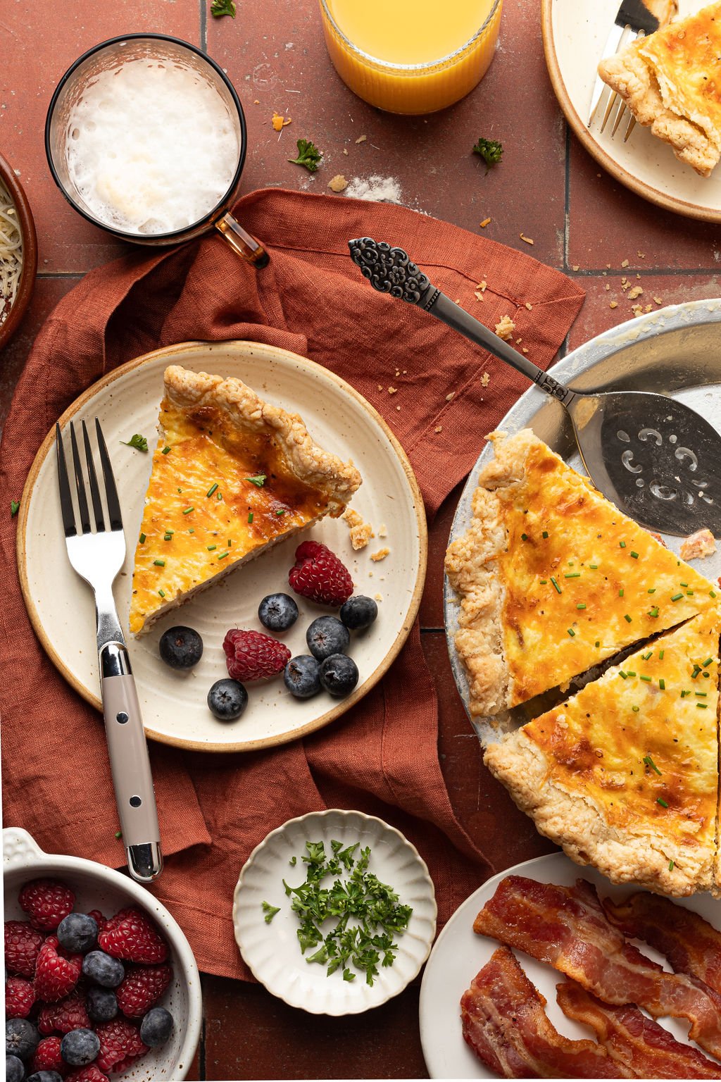 Slice of quiche on a plate with berries next to a pie pan with remainder of quiche and a serving spoon.