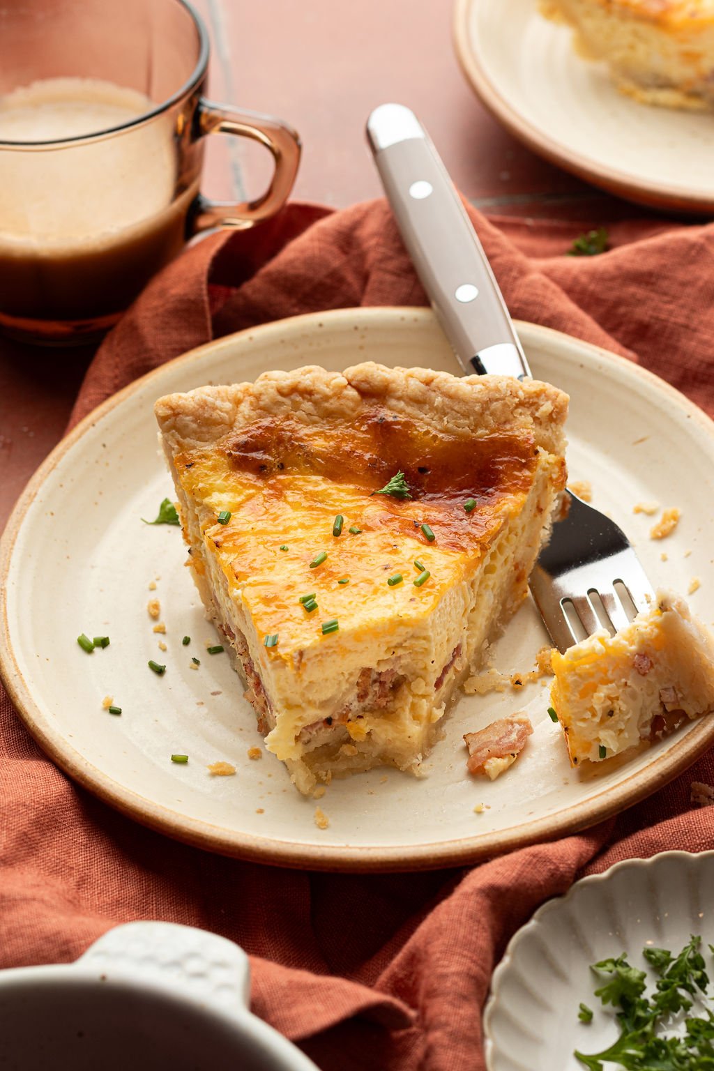 One piece of quiche on a plate with a bite taken out of it and fork resting on the side.