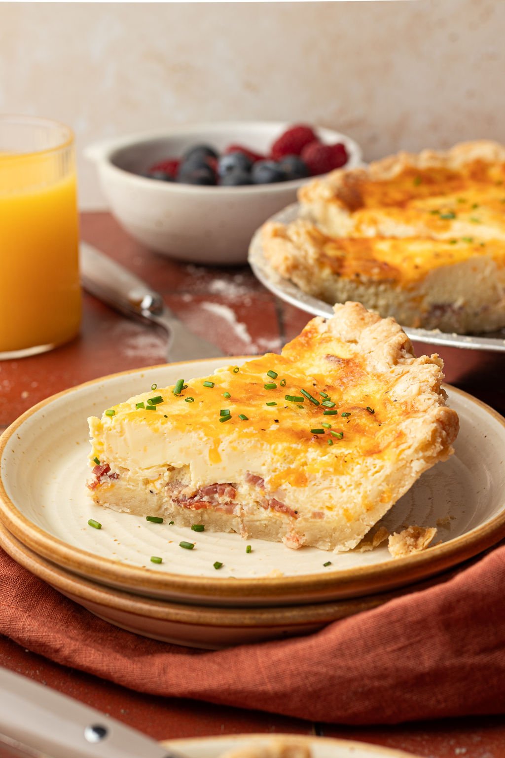 One slice of baked quiche on a plate topped with sliced green onions.