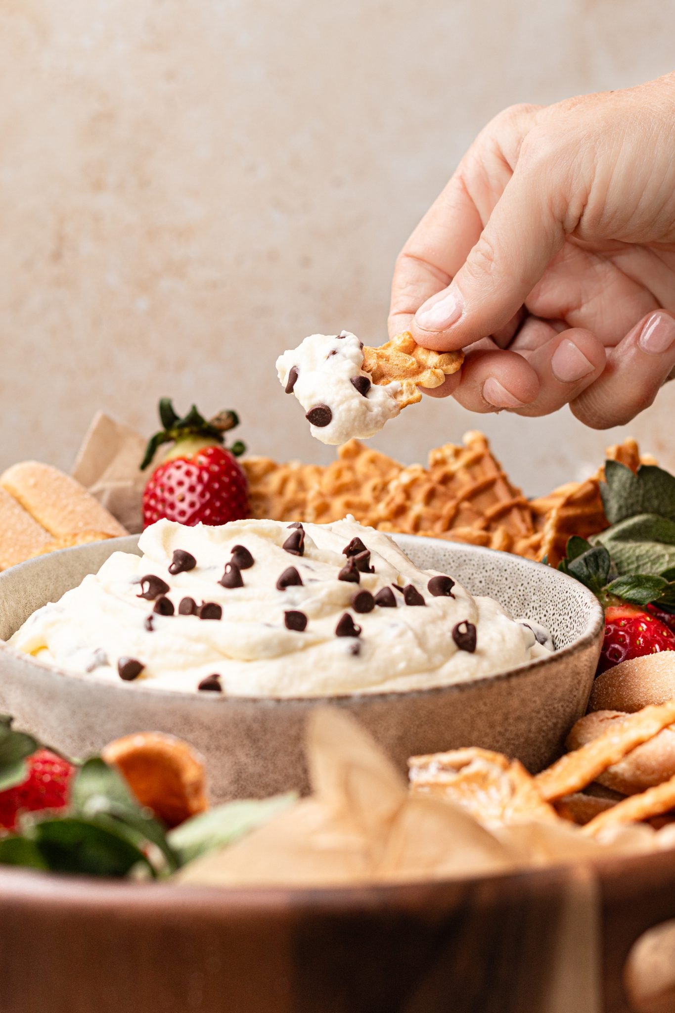 a hand scooping out some cannoli dip with a broken waffle cone. 