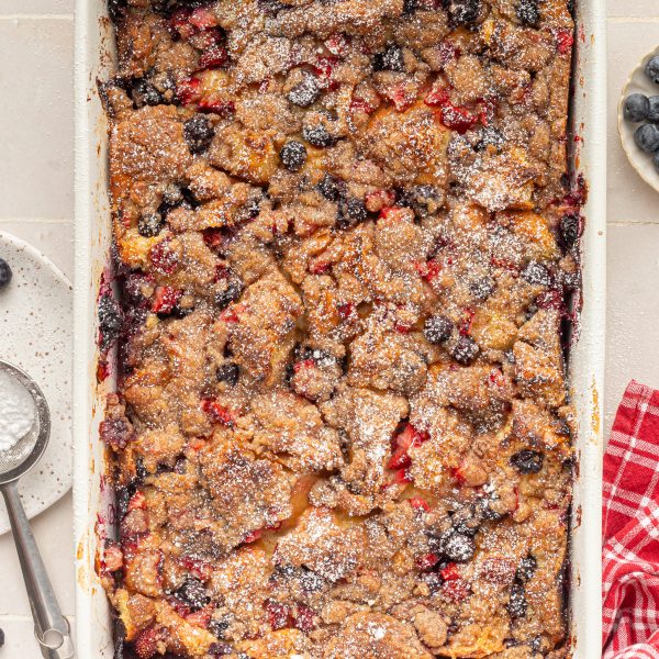 White baking dish with baked french toast with berries, topped with powdered sugar.