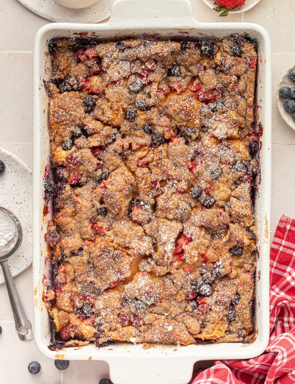 White baking dish with baked french toast with berries, topped with powdered sugar.