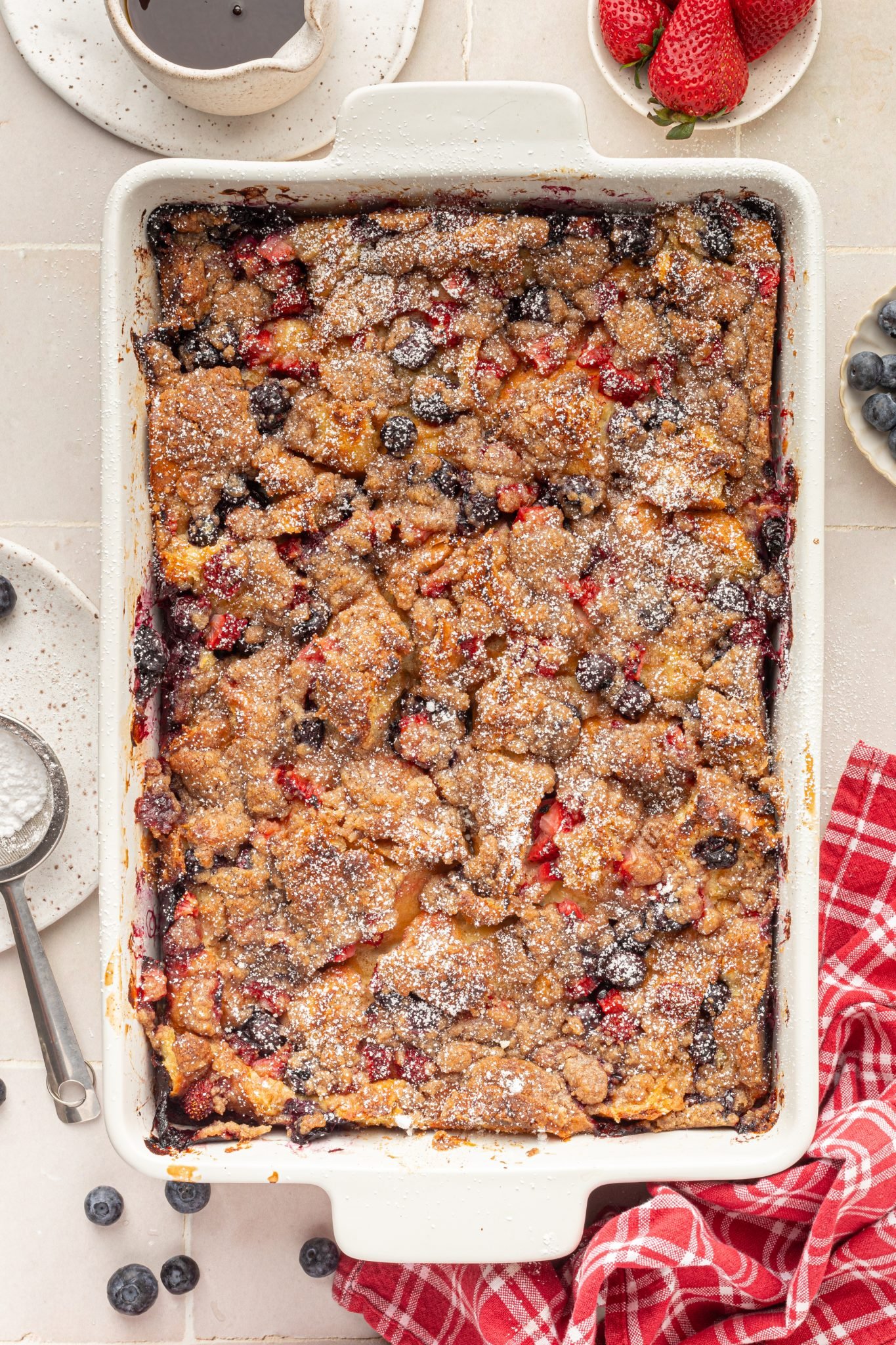 White baking dish with baked french toast with berries, topped with powdered sugar.