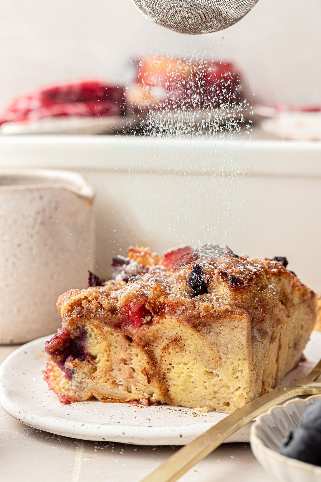 Powdered sugar being sprinkled over a slice of French Toast casserole with berries.