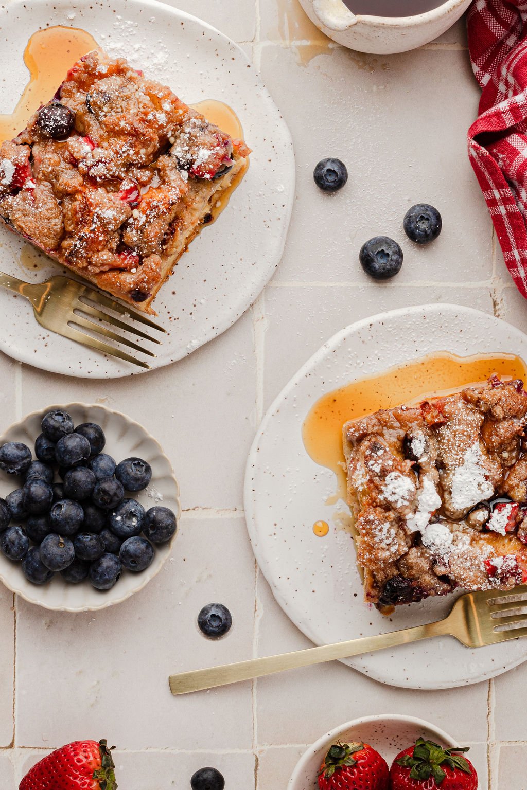 Two plates with slices of a breakfast casserole and a bowl of blueberries.