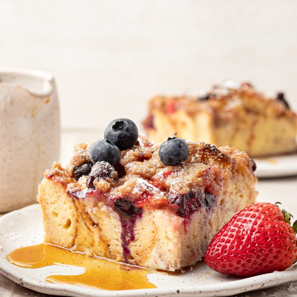 Slice of french toast with strawberries and blueberries with a drizzle of syrup.