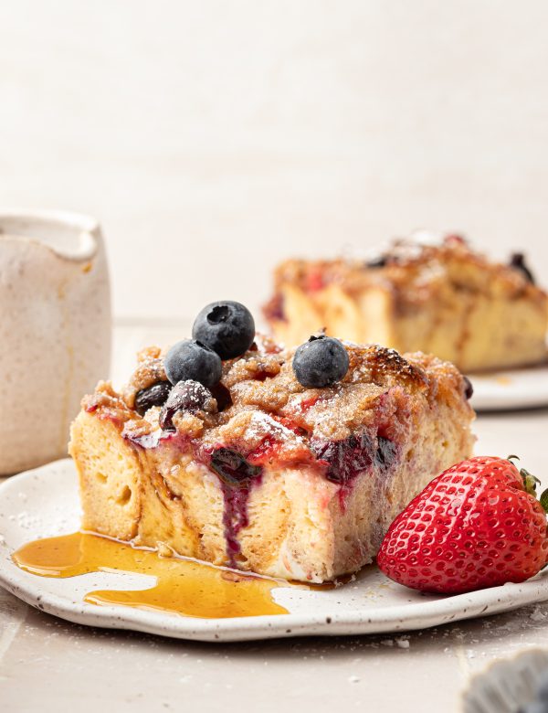 Slice of french toast with strawberries and blueberries with a drizzle of syrup.