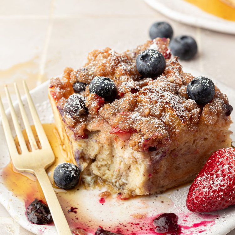 Plate and fork with a slice of a casserole made of French toast filled and topped with berries.