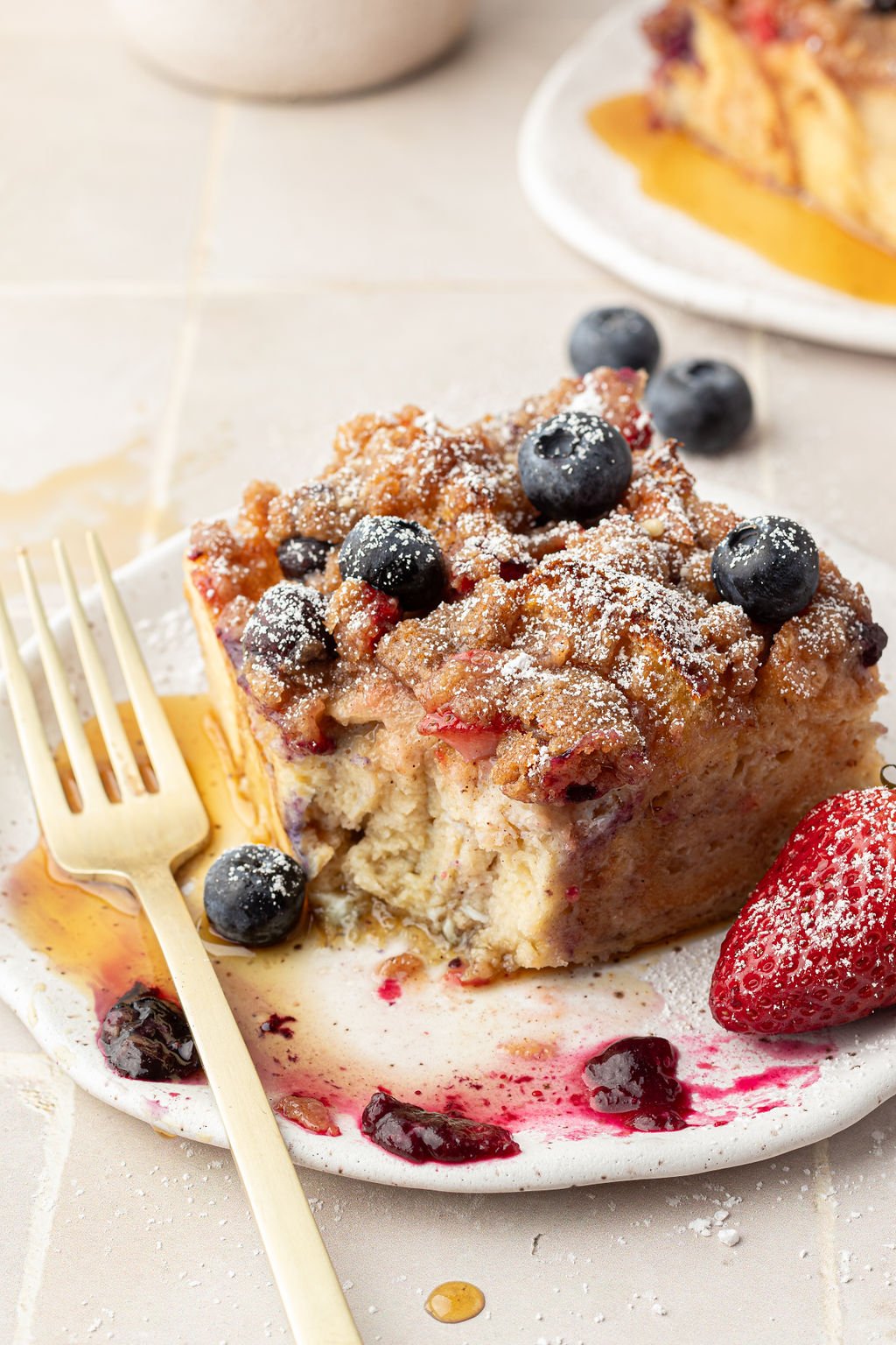 Plate and fork with a slice of a casserole made of French toast filled and topped with berries.