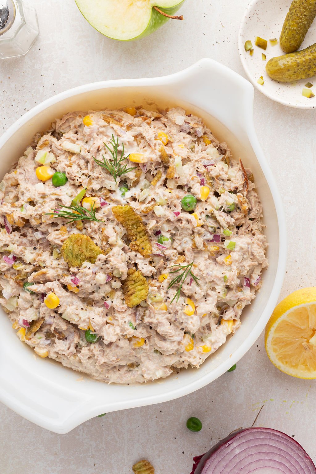 White bowl full of tuna salad with corn, peas, crispy jalapenos, and topped with fresh dill.